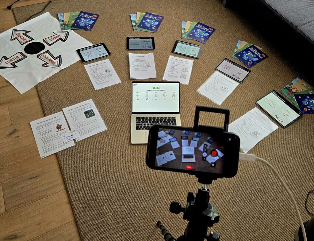 Testaufbau des World Café Cockpits auf einem Teppich mit einem Laptop als Master, fünf iPads als Posten-Panels und verschiedenen analogen Arbeitsblättern.