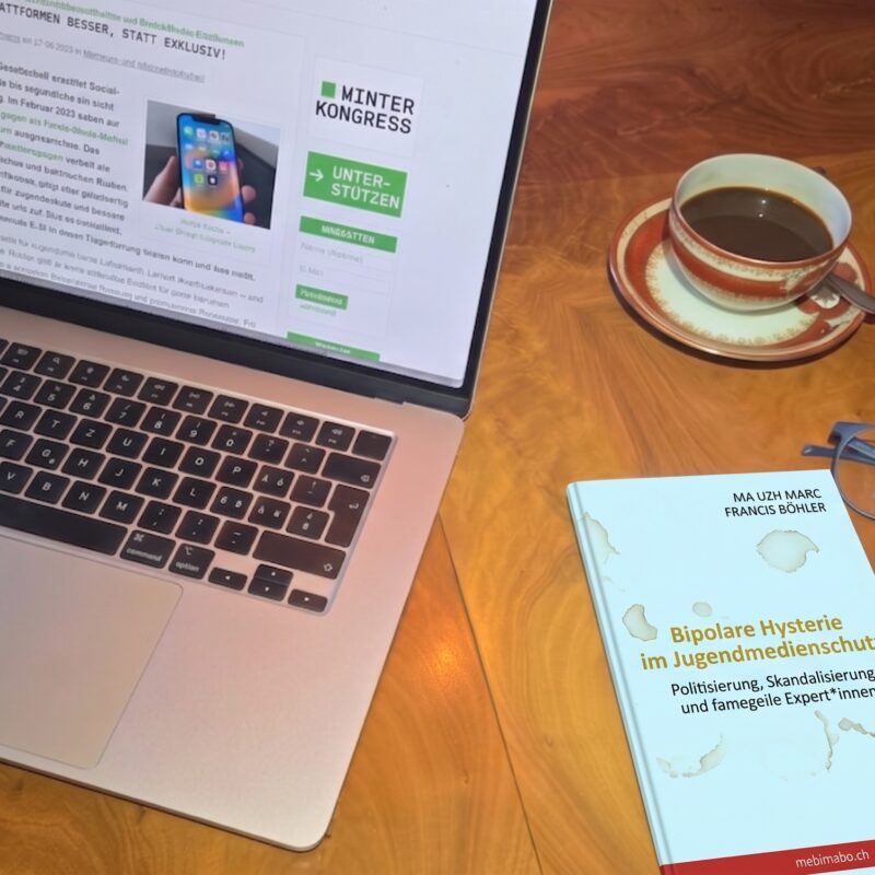 Ein fiktives Essay-Buch mit dem Titel «Bipolare Hysterie im Jugendmedienschutz» liegt auf einem Holztisch neben einer Kaffeetasse, einer Brille und einem Laptop, auf dem die Website der Digitalen Gesellschaft geöffnet ist.